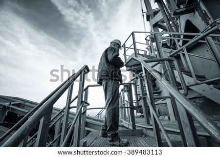 Coal mine worker with a helmet on his head standing in front of huge drill machine and looking at it. Side view. Image is carefully post processed and toned.