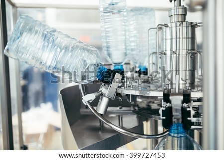 Robotic factory line for processing and bottling of pure spring water into canisters and bottles. Unrecognizable worker in background. Selective focus.