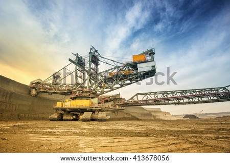 One side of huge coal mining drill machine photographed from a ground with wide angle lens. Mining site and dramatic and colorful sky in background. Low angle shot.