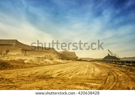 One side of huge mining drill machine connected to transportation facility. Photographed from a ground with wide angle lens. Dramatic and colorful sky in background.