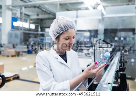 Young happy woman worker in factory checking robotic line for water bottling and packing. Inspection quality control. People at work.