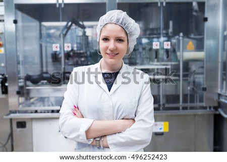 Industrial people. Portrait of smiling young woman in protective working wear. She standing in front of huge line for water bottling.