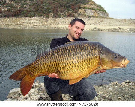 Happy  fisherman holding a giant common carp