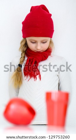 little girl in a red cap with a red apple and a glass on the tab