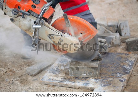 Profile on the blade of an asphalt or concrete cutter and workers boots .Construction worker using a concrete saw, cutting stones in a cloud of concrete dust for creating a track.