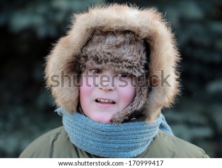 boy cheeks pink winter hat hood in the background of blue spruce