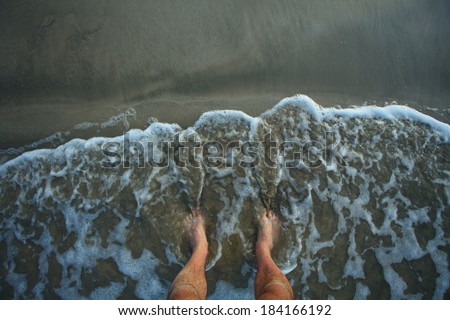 male legs on beach.waves wash the feet of the men on the bank of sand.waves wash the feet of the men on the bank of sand. gray and black sand beach of the Bay of Bengal Passikuda Indian Ocean