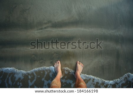 male legs on beach.waves wash the feet of the men on the bank of sand. gray and black sand beach of the Bay of Bengal Passikuda Indian Ocean