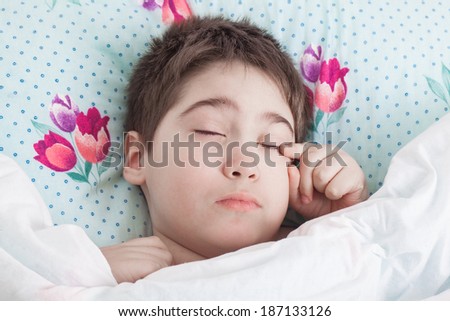 boy is waking up on a pillow in bed under a blanket