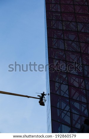 worker cleans glass building climber standing on tap. silhouette wearing a helmet at the height against the sky