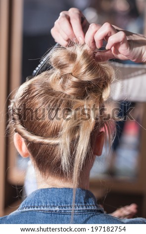 Hair stylist creates on the girl\'s head. Back view Hairdresser makes hairstyle bride