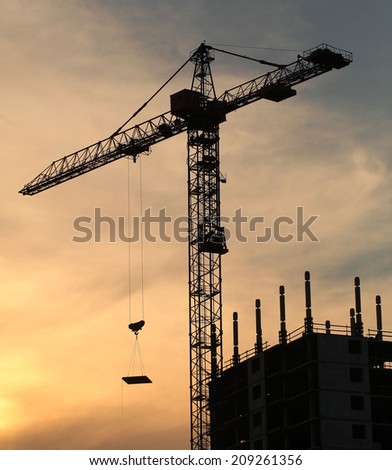 crane lifts the load on a house under construction in the background of a sunset.vertical shot