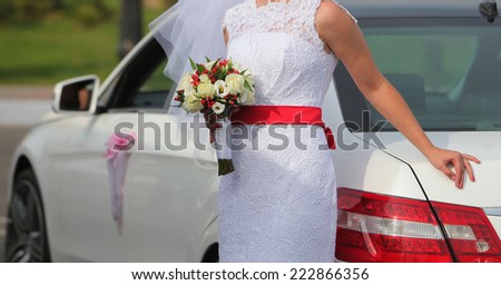 bride with bouquet is standing near the car.holiday flower and red bow