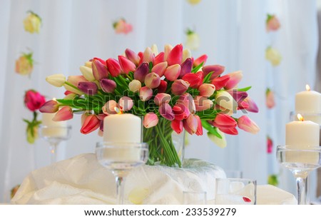 Bouquet of red and yellow tulips on a festive table. Wedding decoration.Burning candles stand. Hanging rosebuds.