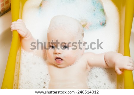 Baby boy age 4 months bathes in a bathroom in the foam is learning to sit.