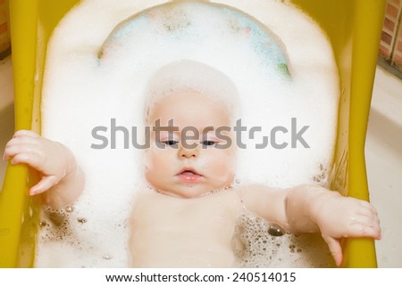 Baby boy age 4 months bathes in a bathroom in the foam is learning to sit.