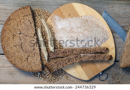 Whole-wheat bread. Corn and wheat ears. Coarse flour on a wooden table.