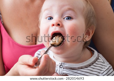 baby feeding spoon of porridge. mouth wide open. maternal care