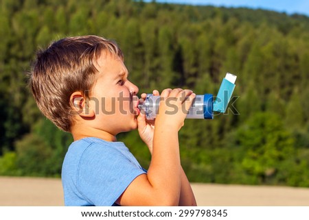 Boy using inhaler for asthma in village with summer sunset and forest