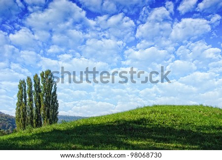 green hill with trees and a blue and cloudy sky in background