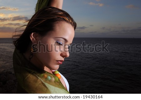Portrait of young fashion female model relaxing by the ocean at sunset
