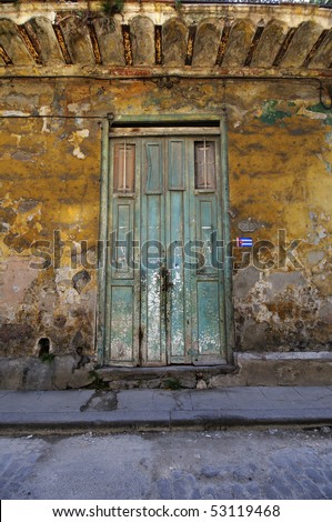 Green rustic door over crumbling walls in eroded building facade in Old Havana, Cuba.