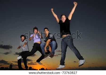 Group of four young males jumping against sunset sky background with happy expression