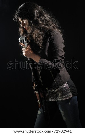 Portrait of young brunette beauty singing with retro microphone isolated on black
