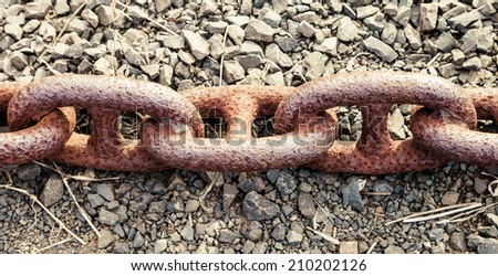Three ancient links rusted together of a large old shipping anchor chain lying discarded on gravel with dry grass