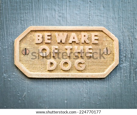 Old and weathered brass sign with letters BEWARE OF THE DOG and geometric pattern screwed into hand painted grey wood gate