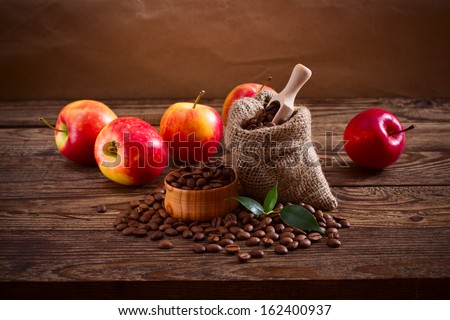 Coffee beans in a bag, scattered on a wooden table and a number of red apples. Free space for your text