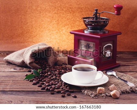 Cup of Warm Coffee, Sugar and Grinder. Coffee Beans scattered on Wooden Surface. Free space for your Text