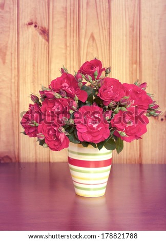 Beautiful bouquet of flowers in vase on wooden table old. Vintage red roses in retro style. Wooden surface.