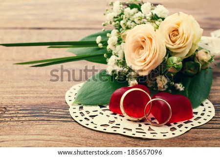 Bridal bouquet of white flowers on wooden surface. Summer wedding day, unusual designer florist bouquet of delicate roses. Wedding rings.  Free space for text.