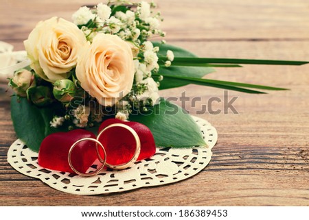 Bridal bouquet of white flowers on wooden surface. Summer wedding day, unusual designer florist bouquet of delicate roses. Wedding rings, couple, heart . Free space for text.