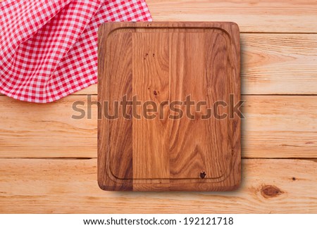Empty kitchen cutting board. Wooden table covered with red checked tablecloth. View from top.