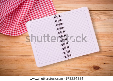 Pure notebook for recording menu, recipe on red checkered tablecloth tartan. Wooden table close up view from top