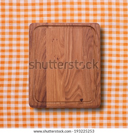 Wooden table covered with checked tablecloth. View from top. Empty kitchen cutting board on a background of the tablecloth for product installation. Space for text