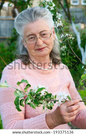Portrait of serene mature woman in garden. Senior woman relaxing outdoors hold flowers in hands.