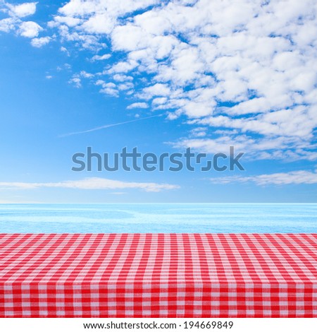 Empty wooden deck table with tablecloth for product montage. Sunny day, blue sky with clouds, sea, coast. Free space for your text