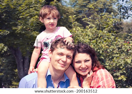 Happy mother, father and daughter in the park. Happy family. Parents giving child piggybacks in countryside. Summer landscape