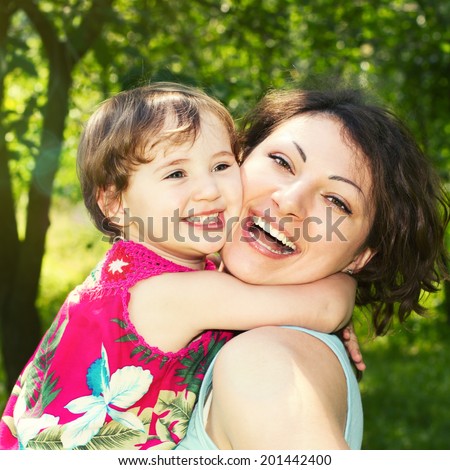 Portrait of happy little girl who embraces his mother. Face of beautiful mother and daughter close-up. Outdoor portrait of happy family. Joy mom and baby.