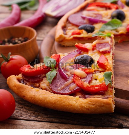 Food.  Pizza with tomato, salami and olives. Pizza with ham, pepper and olives. Delicious fresh pizza served on wooden table.