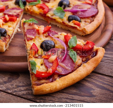 Food.  Pizza with tomato, salami and olives. Pizza with ham, pepper and olives. Delicious fresh pizza served on wooden table.