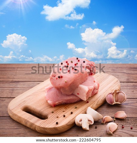 Raw meat for barbecue with fresh vegetables and mushroom wooden surface. Food, meat raw steak, beef steak bbq, spices for cooking meat. Background blue sky with clouds and sun