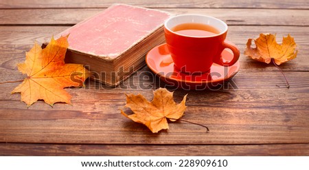 Cup of tea with autumn leaves reflection on book on wooden table. Season of Education