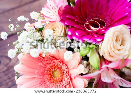 Wedding bridal bouquet of white roses and pink lilies with wedding rings on wooden table, macro
