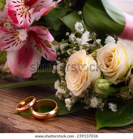 Wedding bridal bouquet of white roses and pink lilies with wedding rings on a wooden table, close-up