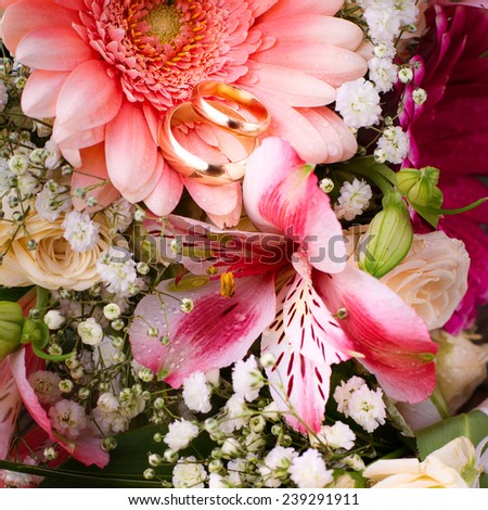 Wedding bridal bouquet of white roses and pink lilies with wedding rings on a wooden table, close-up