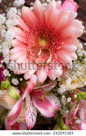 Wedding bridal bouquet of white roses and pink lilies with wedding rings on  wooden table, close-up